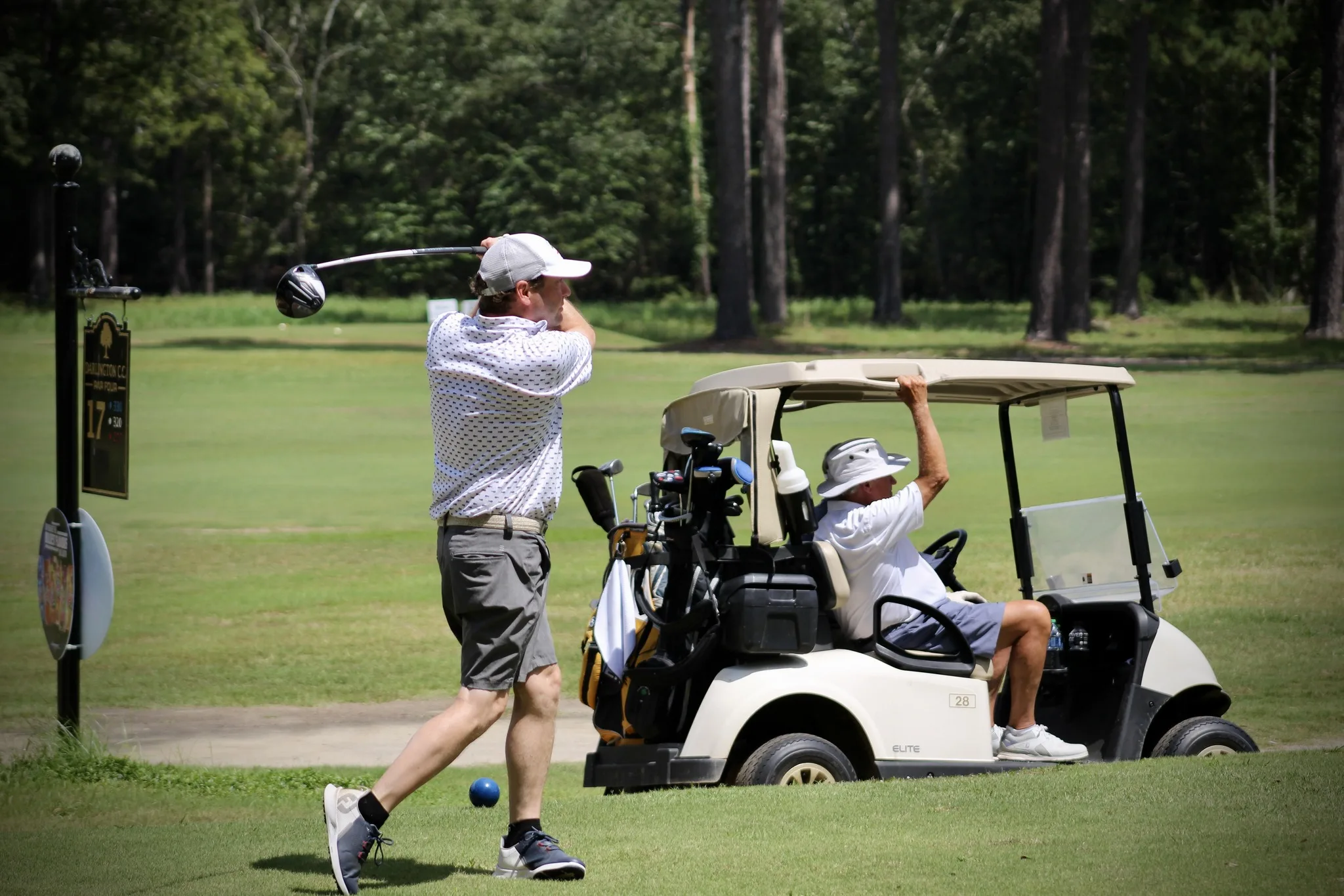 Golfer swinging his club as a golf cart passes by at Darlington Country Club