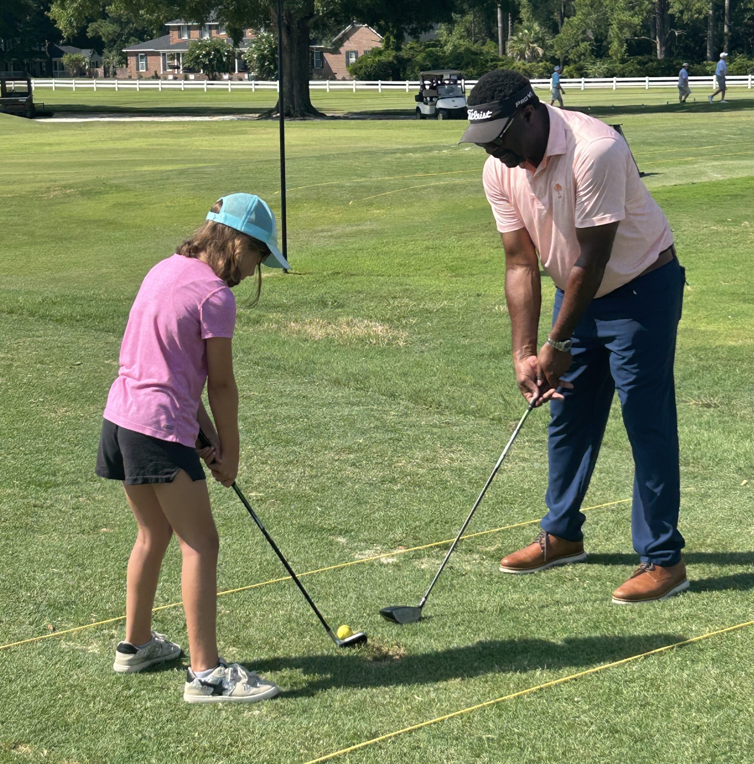A man teaches a young girl how to swing a golf club on a sunny golf course.